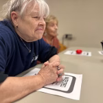 A woman sits with her hand folded in front of her listening intently to a person off camera.