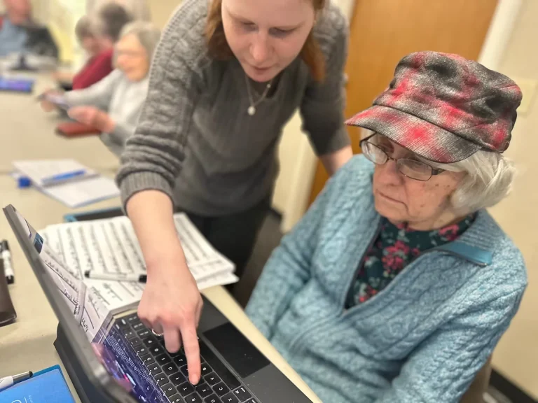 A woman shows another woman a key on a laptop computer.