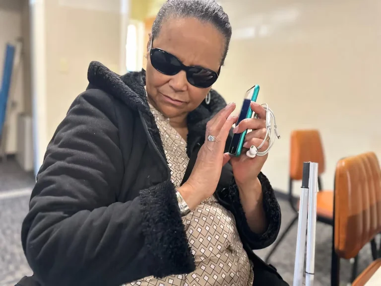 A woman wearing sunglasses holds her smartphone near her face and listens to what it is communicating.