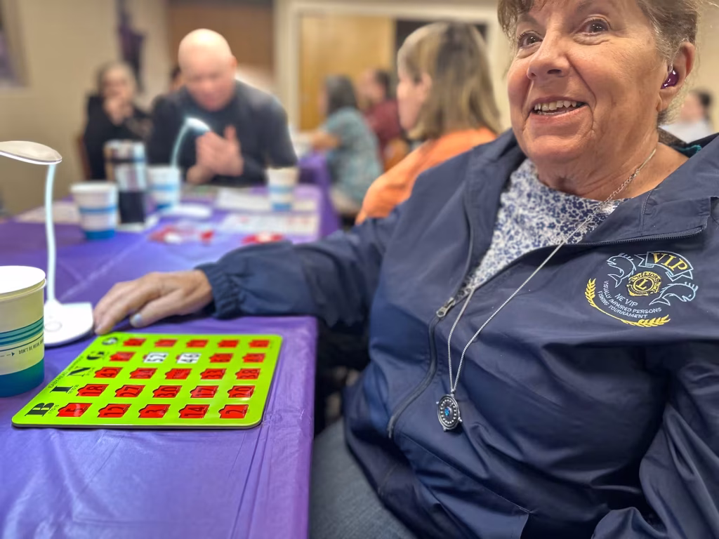 A women sits at a table and a large print bingo card sits in front of her.