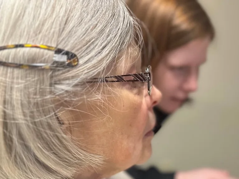 A woman's face looking foward with a second person in the background pointing to something.
