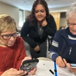 Two women sitting a table look at their iphones.