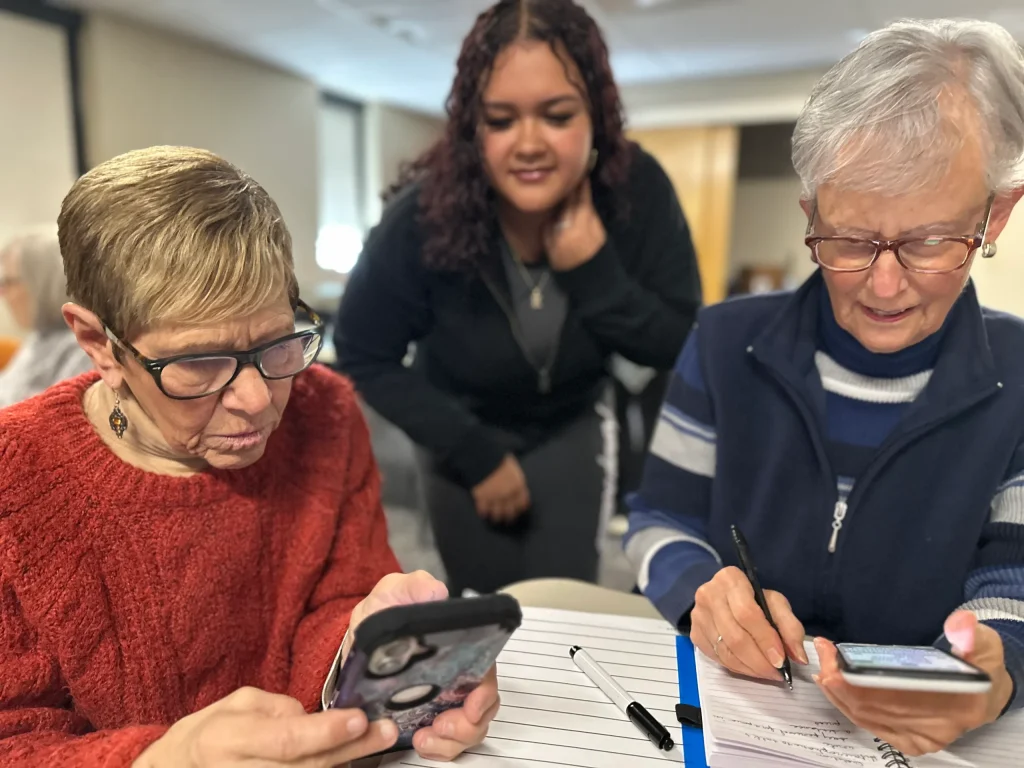 Two women sitting a table look at their iphones.