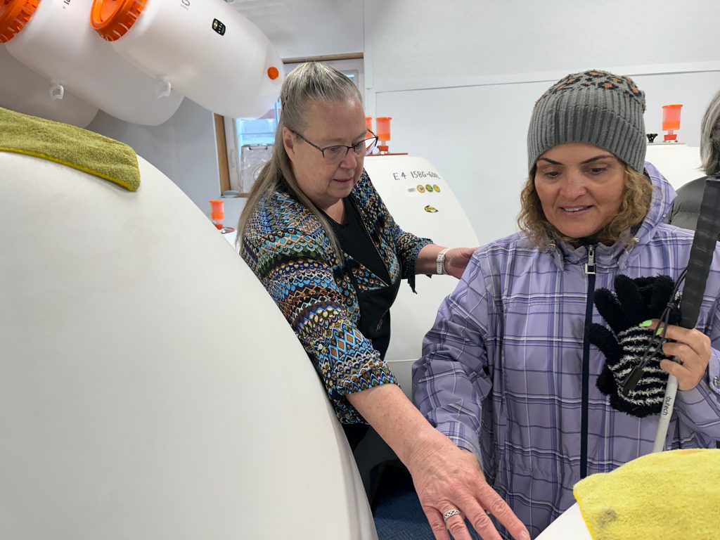 IMG_4280 - IN-SIGHT A guide tactically shows a woman who is blind a large wine storage container with her hand.