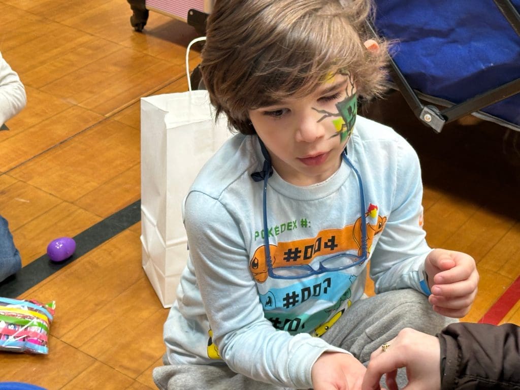 A boy with face paint sits on a floor