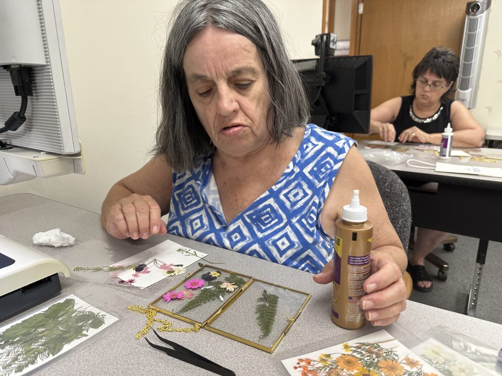 A woman holding a bottle of glue looks at a glass frame containing pressed flowers