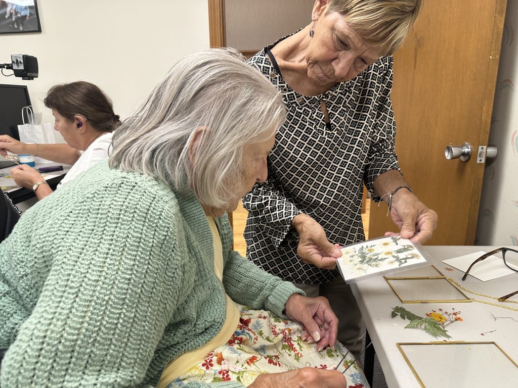 A woman shows another woman a card containing pressed flowers