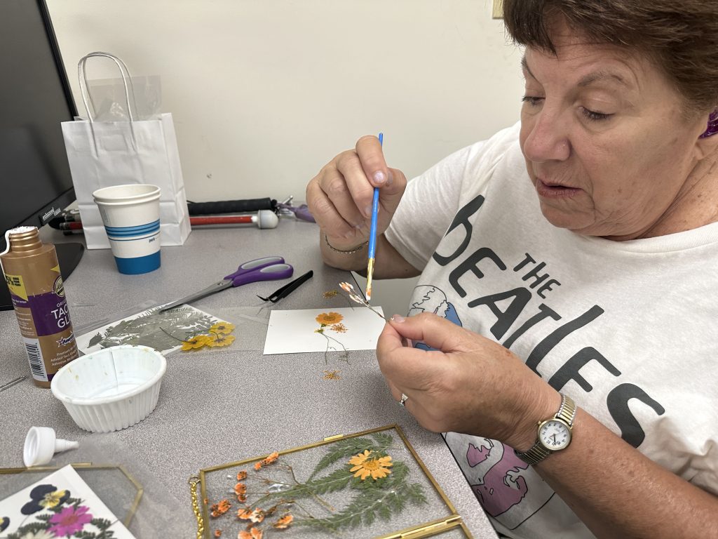 A woman gluess pressed flowers on a glass frame