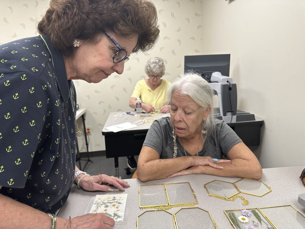 A woman shows another woman a card containing pressed flowers