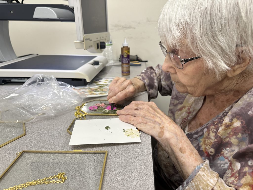 A woman places pressed flowers on a glass frame using tweezers