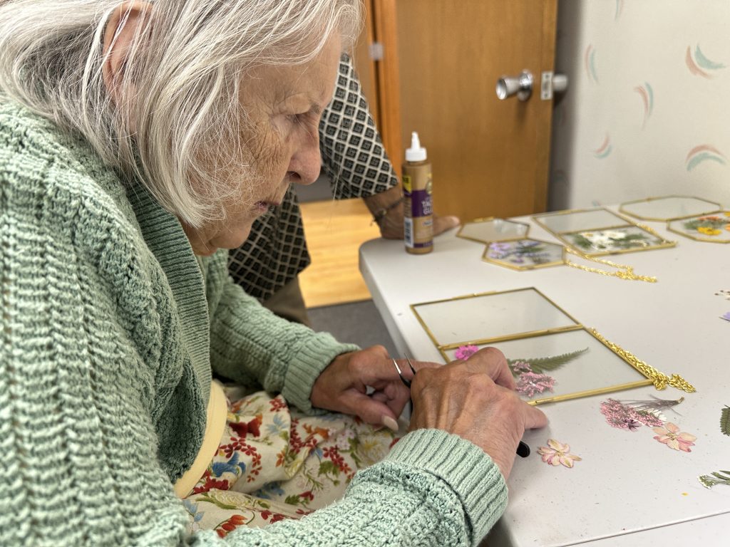 A woman places pressed flowers on a glass frame using tweezers