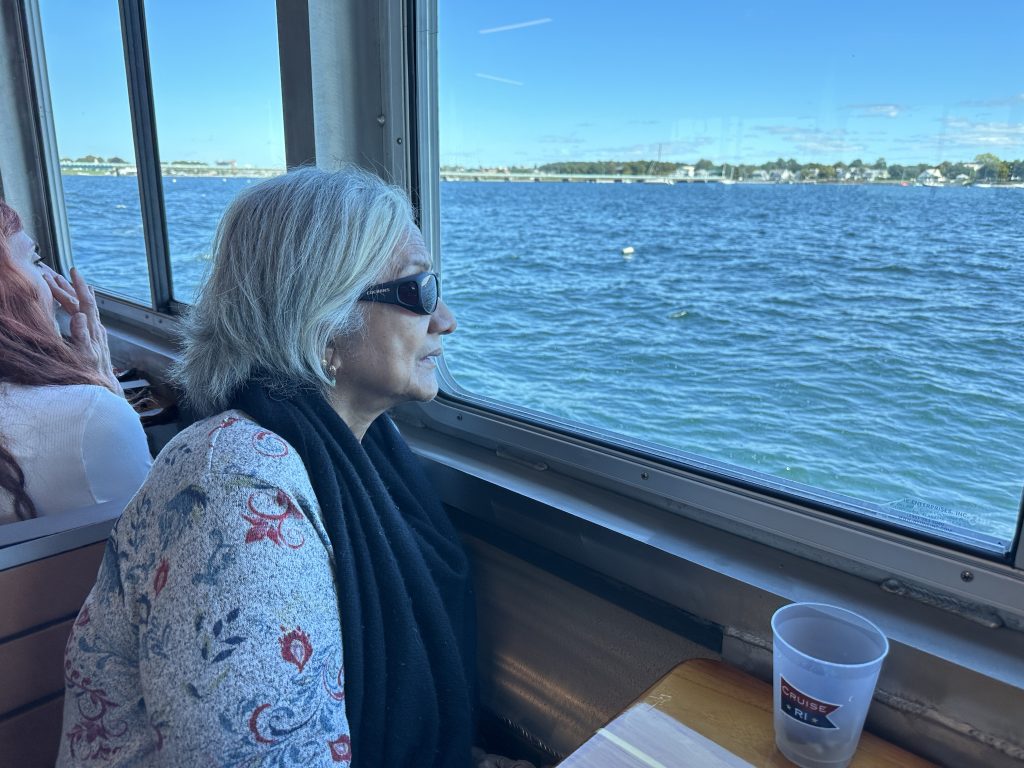 IMG_6990 - IN-SIGHT A woman, sitting at a table on a boat, looks out the window at the water